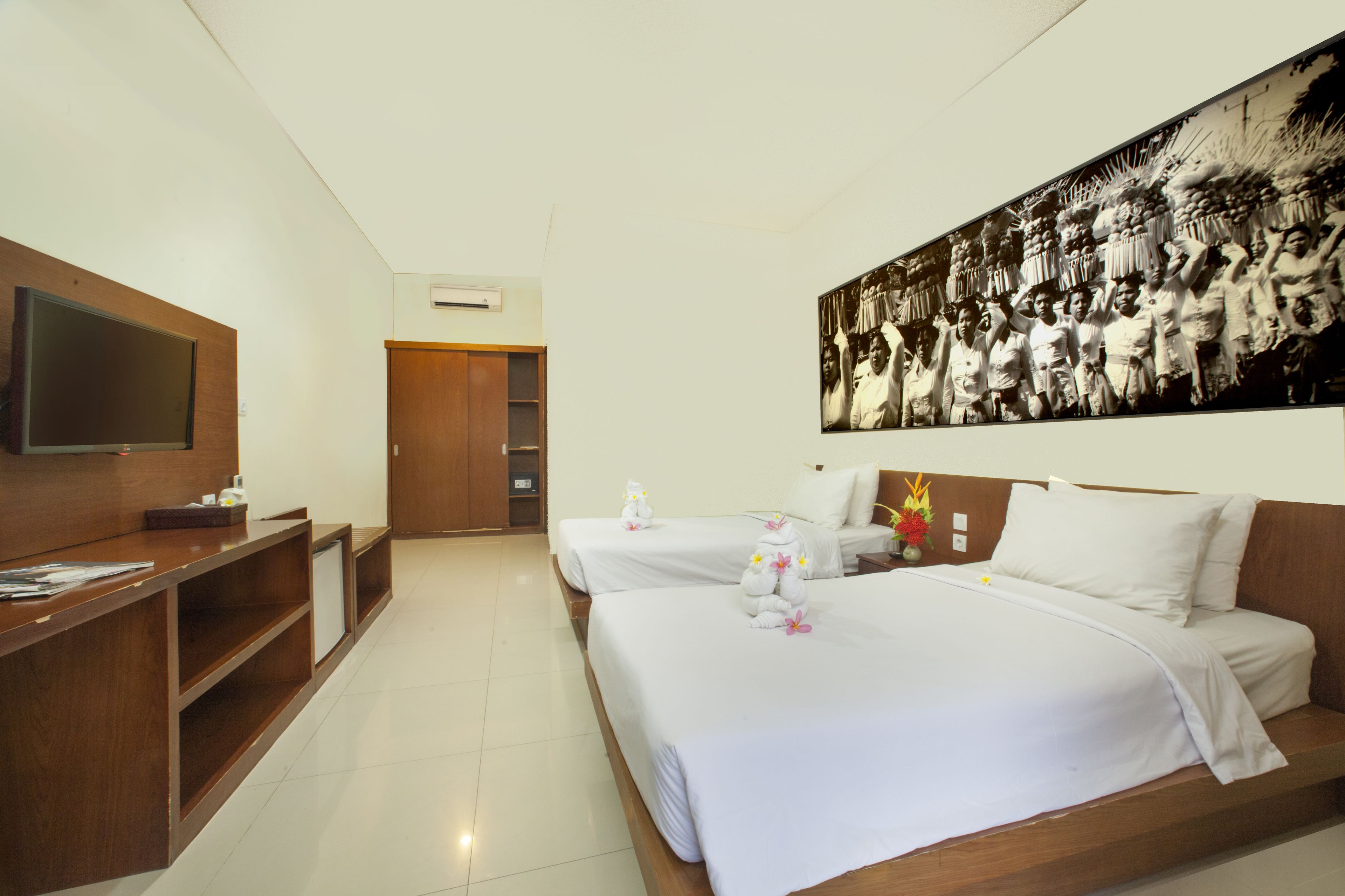 A hotel room with two beds, a flat-screen TV, a wooden desk, and a large black-and-white photo on the wall.
