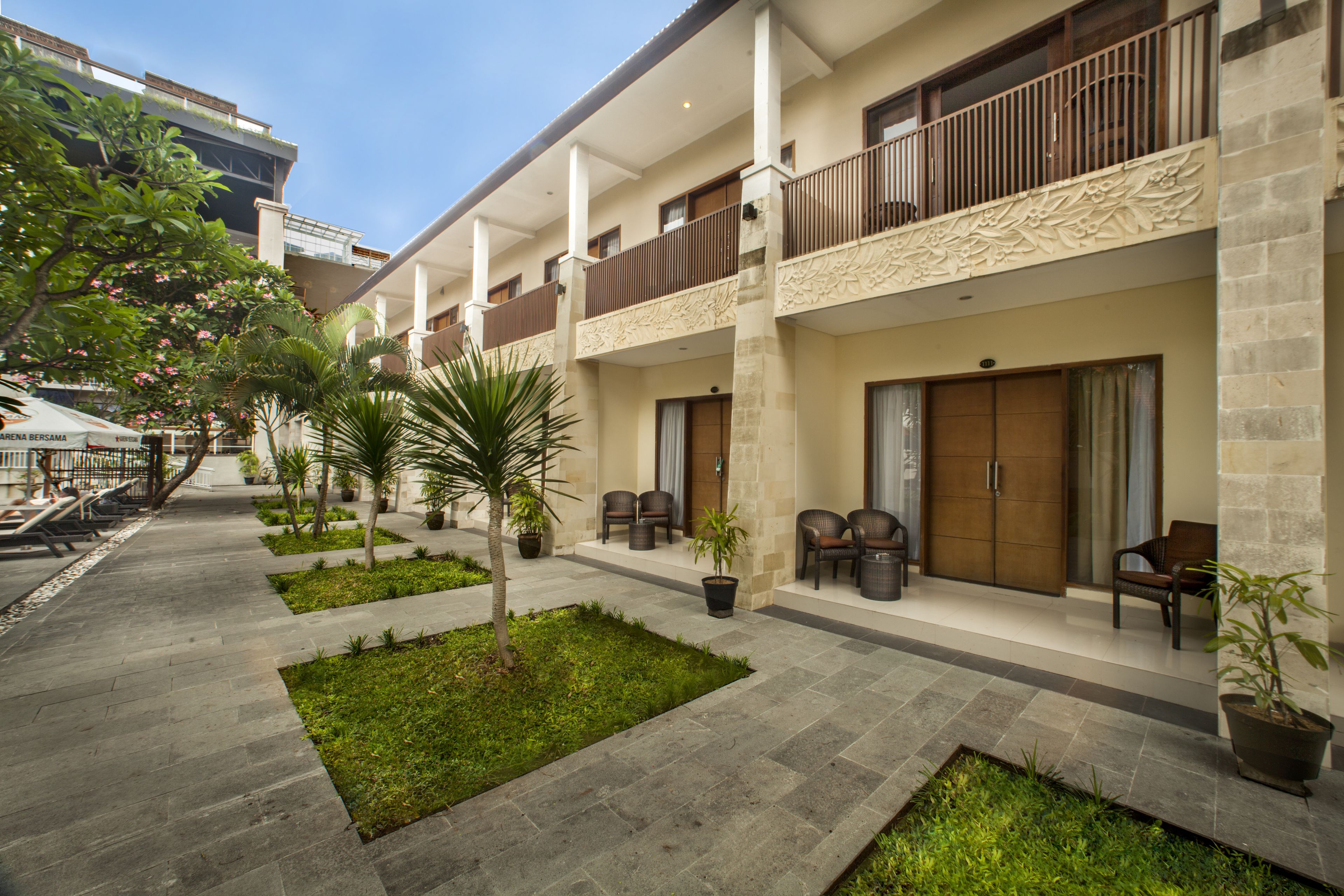 A hotel courtyard with outdoor seating, palm trees, and a stone pathway.