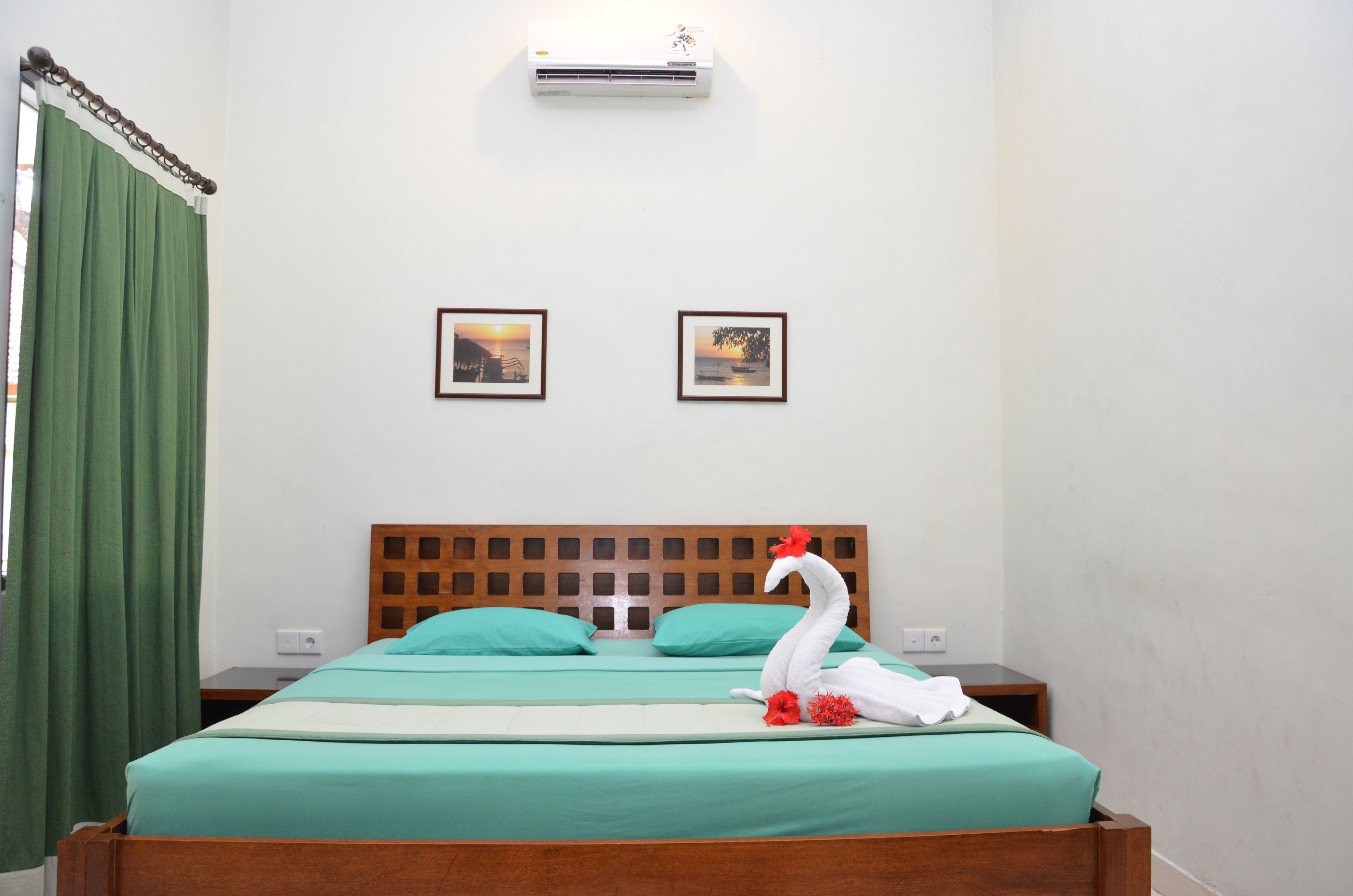 Habitación de hotel con cabecera de madera, ropa de cama verde, una decoración con forma de cisne y dos cuadros en la pared.
