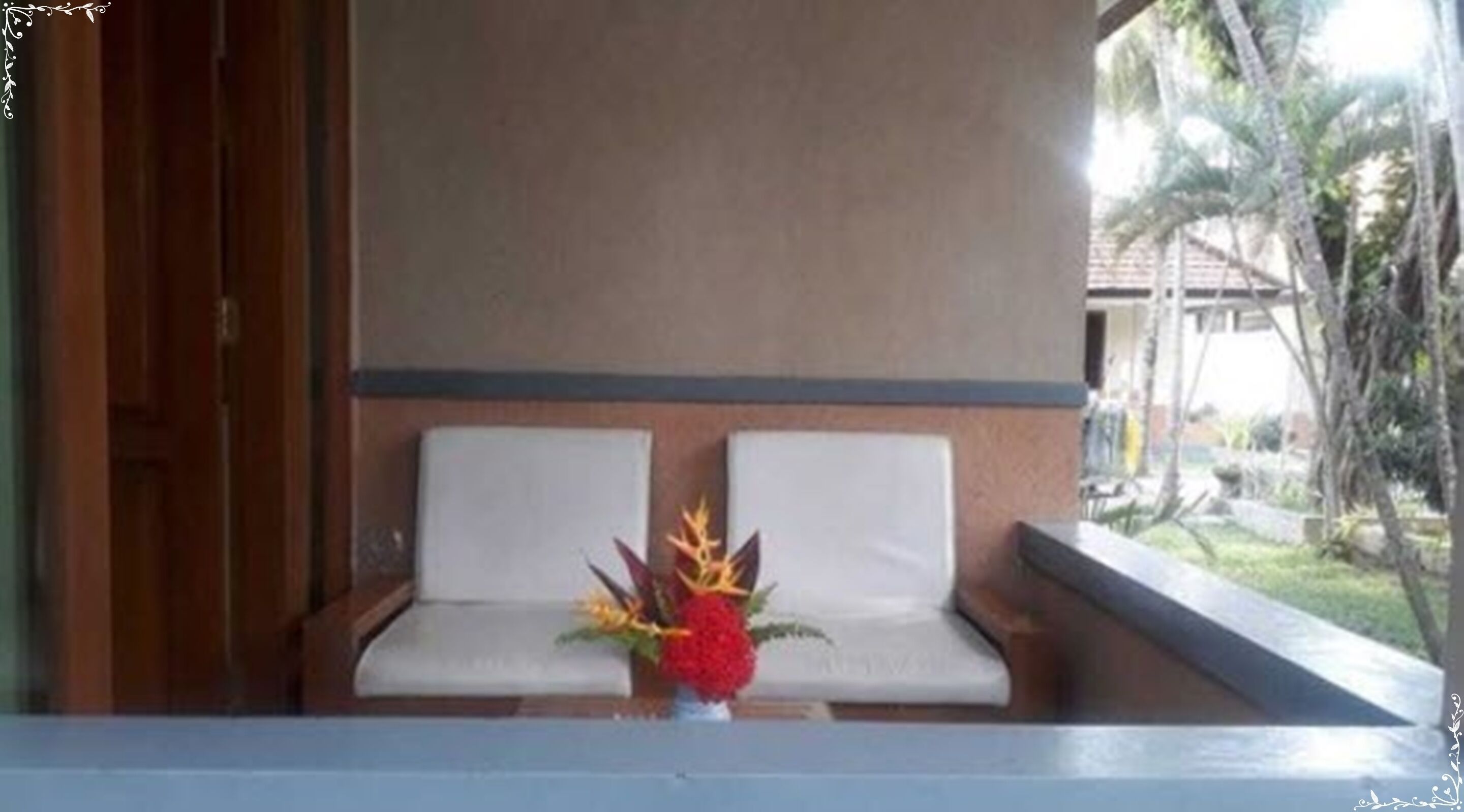 A seating area with two white cushioned benches, a vase with flowers, and a view of a garden.