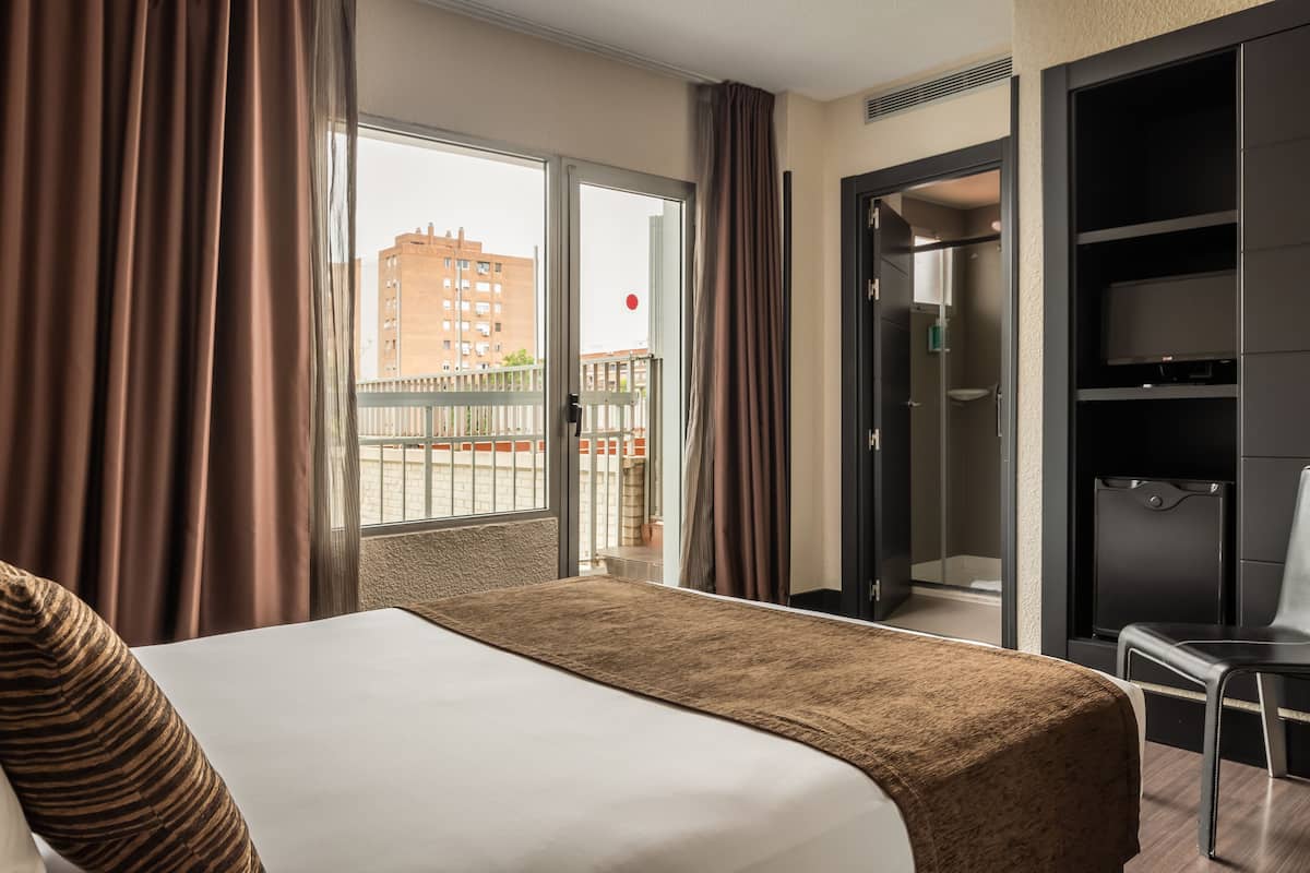 Ein Hotelzimmer mit einem großen Bett, einem Kleiderschrank und Blick auf ein Gebäude durch das Fenster.