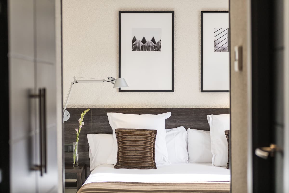 Ein Hotelzimmer mit Bett, Nachttisch, Lampe und zwei gerahmten Bildern an der Wand.