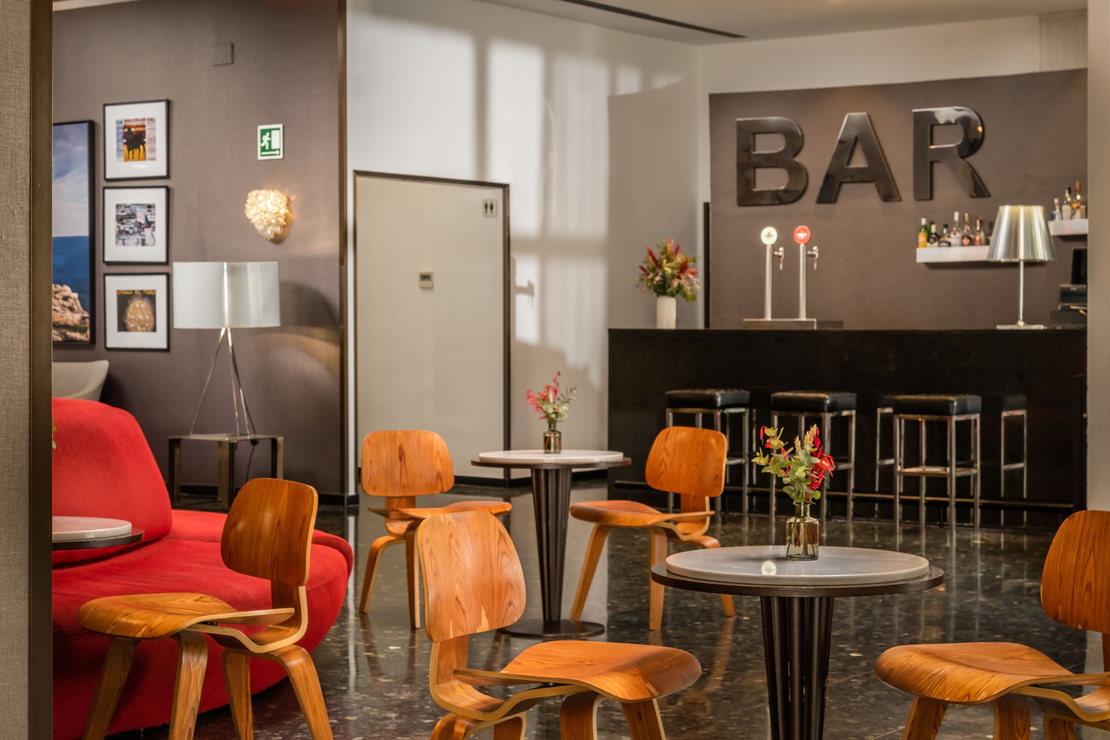 A modern bar area with wooden chairs, a red sofa, and a bar counter with bottles.