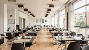 Un comedor amplio con mesas largas, sillas negras e iluminación colgante moderna.