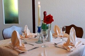 A dining table set for four with a candle, a vase with a red rose, and a bottle of champagne.