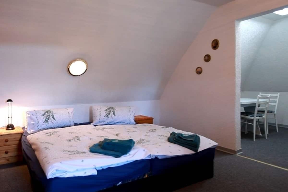 A bedroom with a bed, bedside table, lamp, and a desk with chairs.