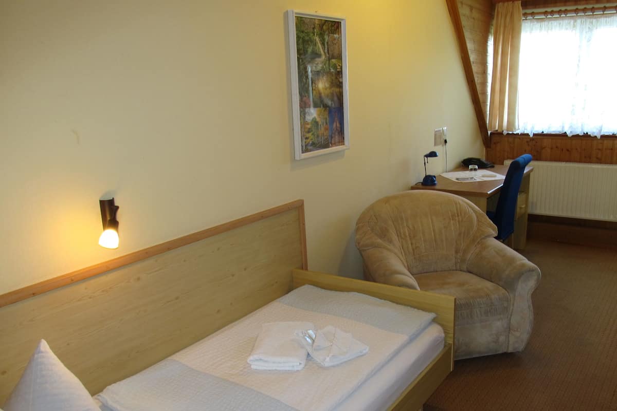A hotel room with a wooden bed, a chair, a desk with a phone, and a painting on the wall.