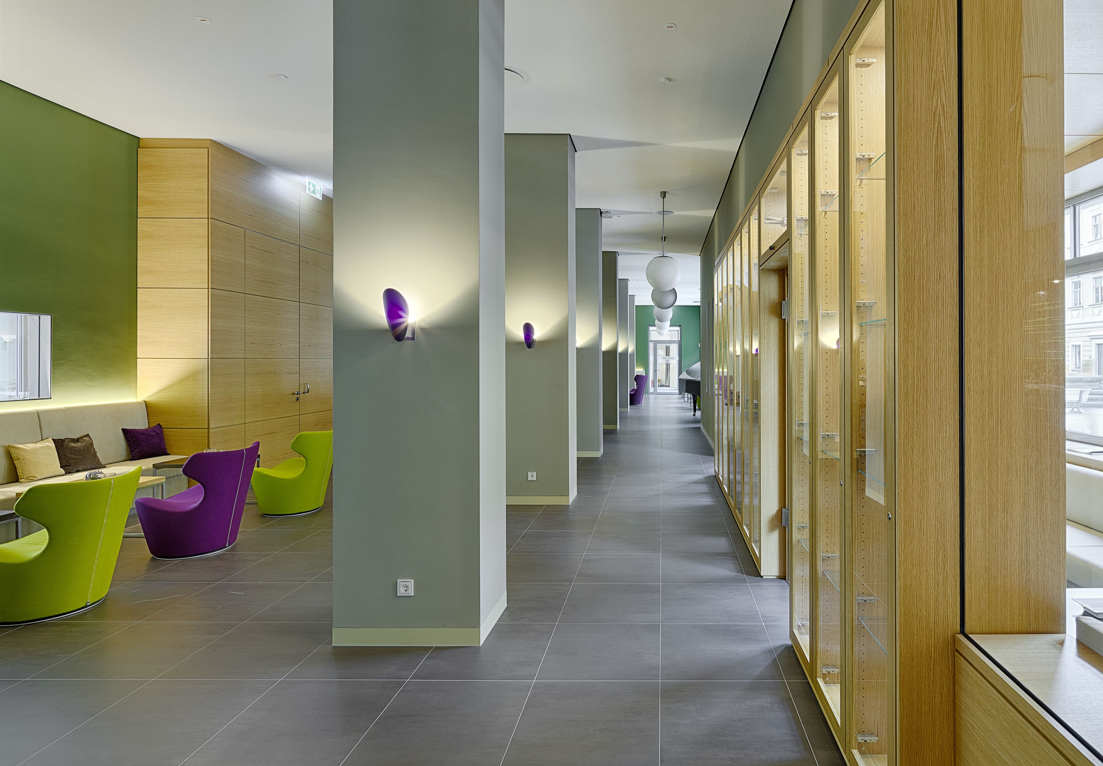 A modern hotel lobby with green and purple seating, a long corridor, and wooden cabinets.