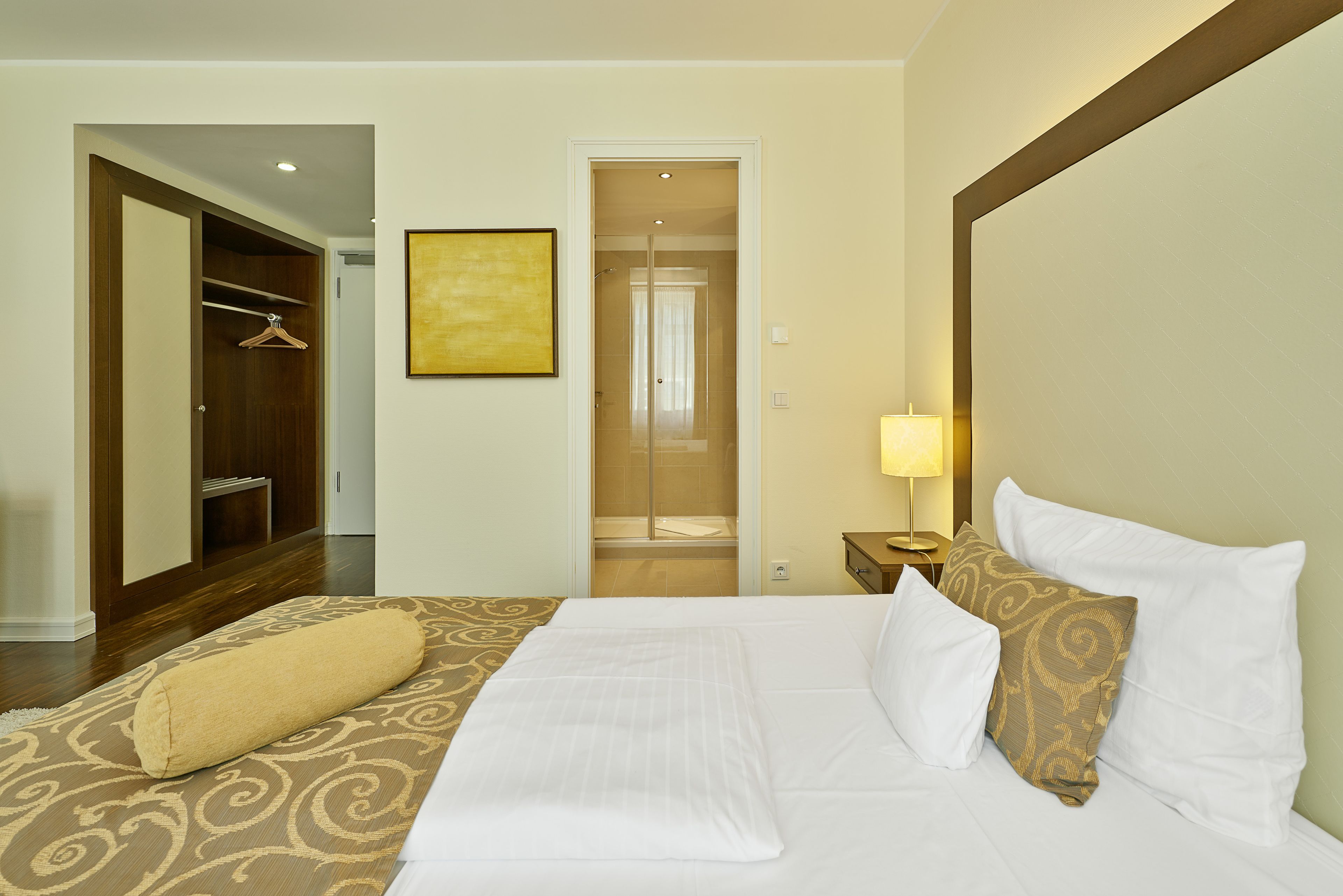 A hotel room with a neatly made bed, a walk-in closet, and a bathroom visible through an open door.