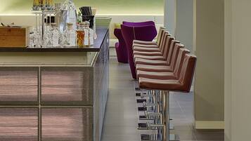 A modern bar area with a central island, bar stools, a purple chair, and a TV mounted on the wall.