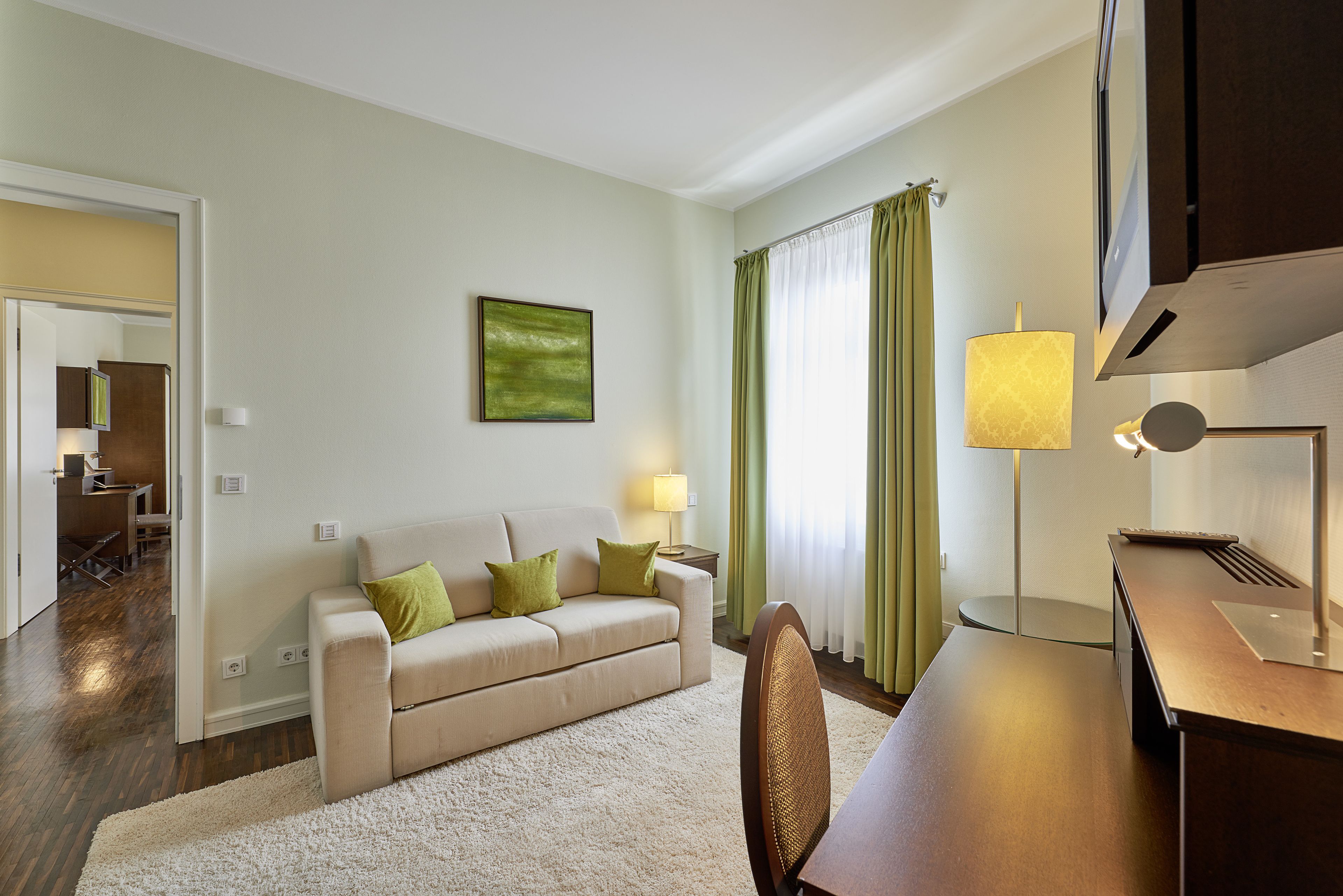 Una sala de estar moderna con un sofá color beige, cojines verdes, una mesa de centro de madera y una lámpara.