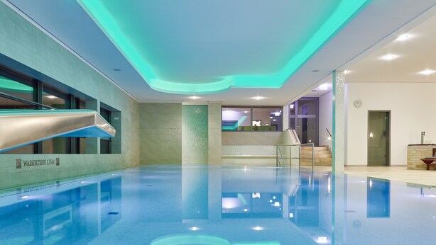 An indoor swimming pool with a clear water surface, a slide, and a reception area with a clock. - Hotel Elbresidenz an der Therme Bad Schandau (Bad Schandau)