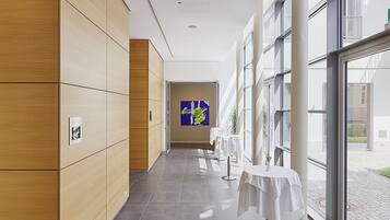 A modern hallway with wooden paneling, a blue artwork on the wall, and tables with white tablecloths.