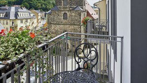 A balcony with a wrought iron table, a stone tower with a clock, and a view of a hill. - Hotel Elbresidenz an der Therme Bad Schandau (Bad Schandau)