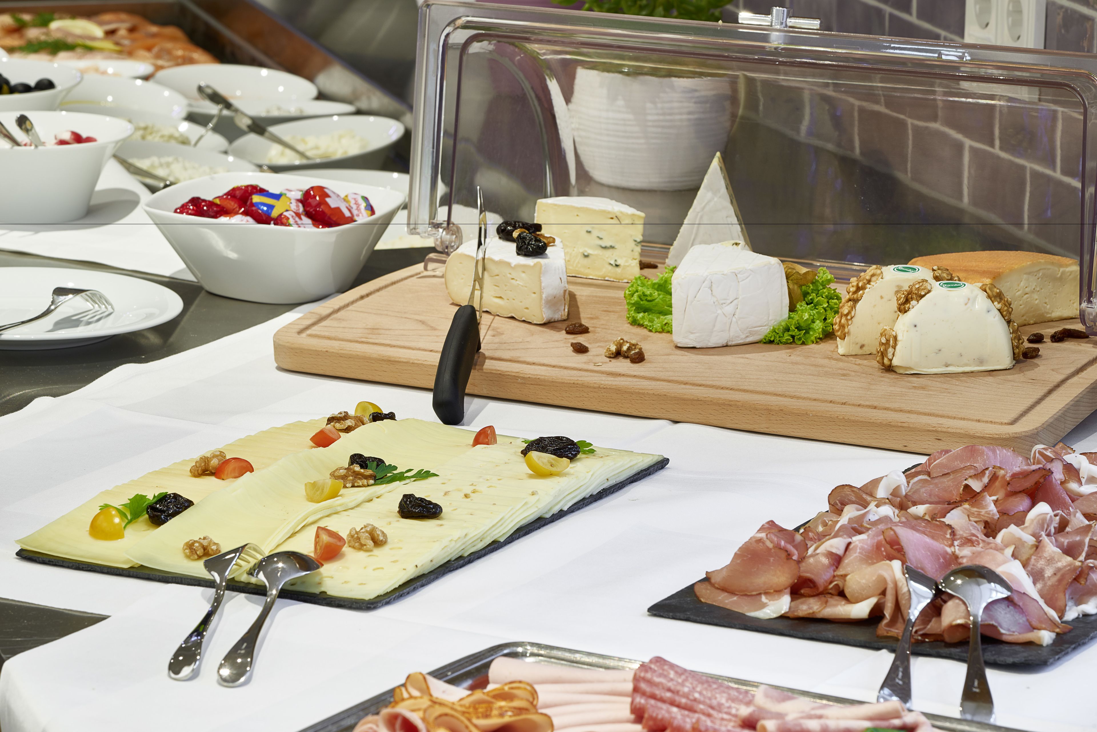 A buffet with various cheeses, fruits, and meats.