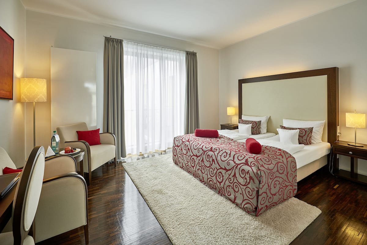 A hotel room with a large bed, a desk with a chair, a sofa, and a large mirror.