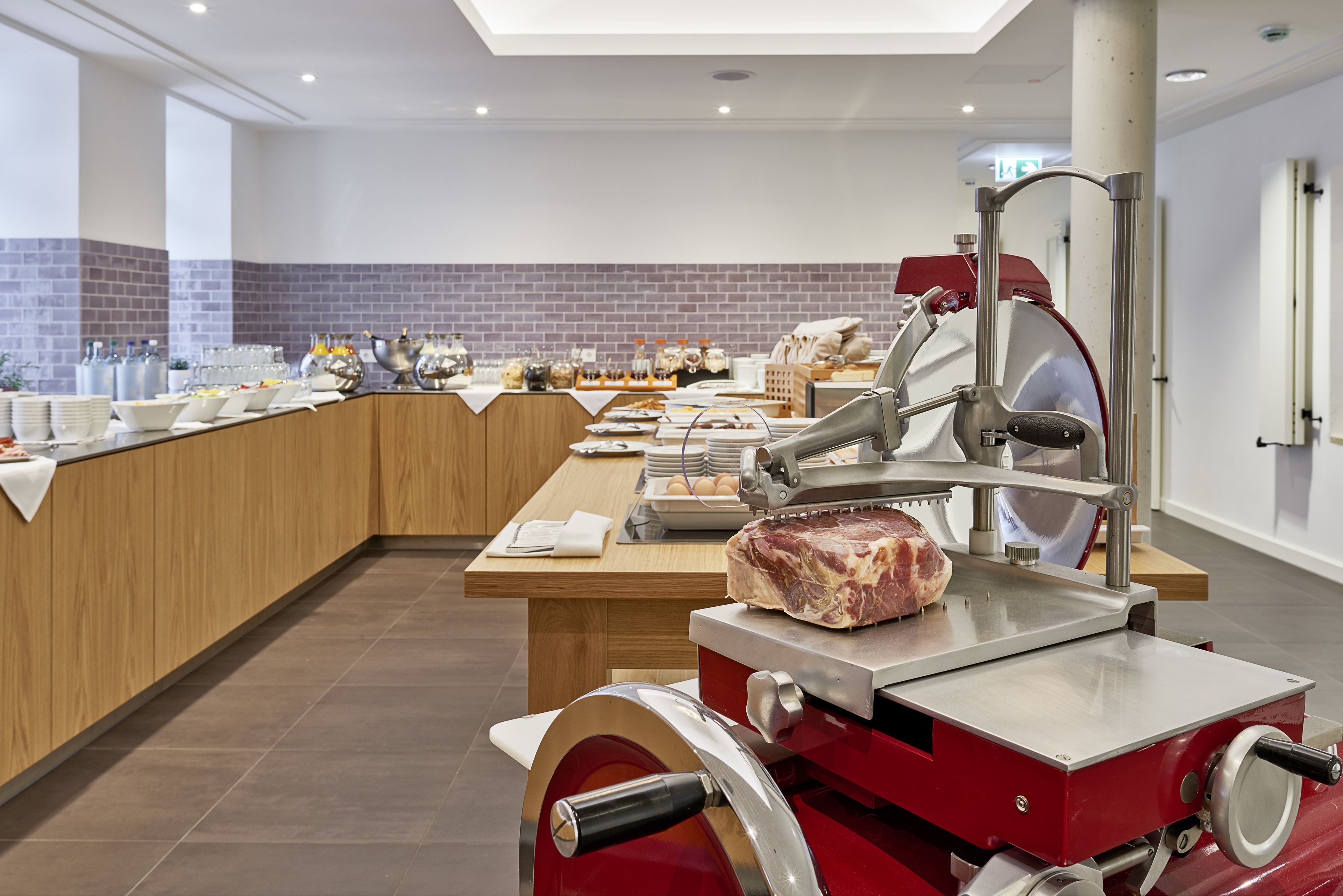 A kitchen area with a meat slicer, a buffet setup with plates, bowls, and condiments.