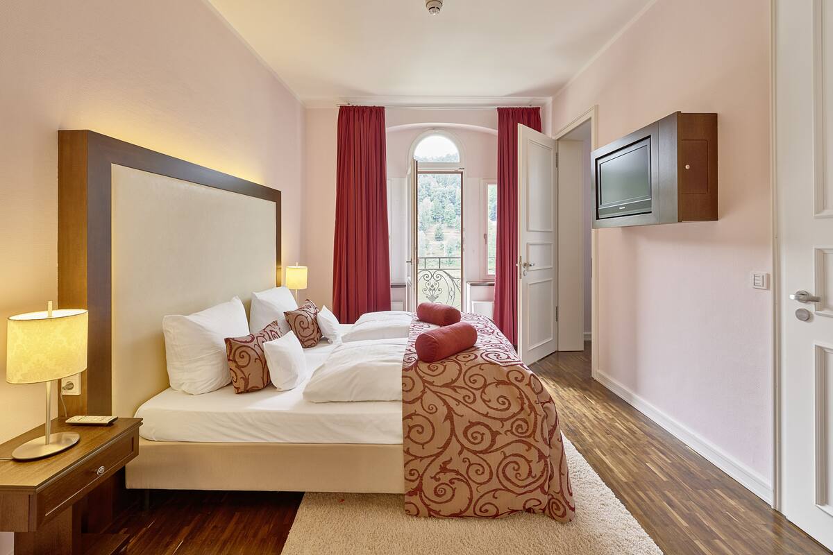 A hotel room with a large bed, a TV mounted on the wall, and a view of the outdoors through a door.