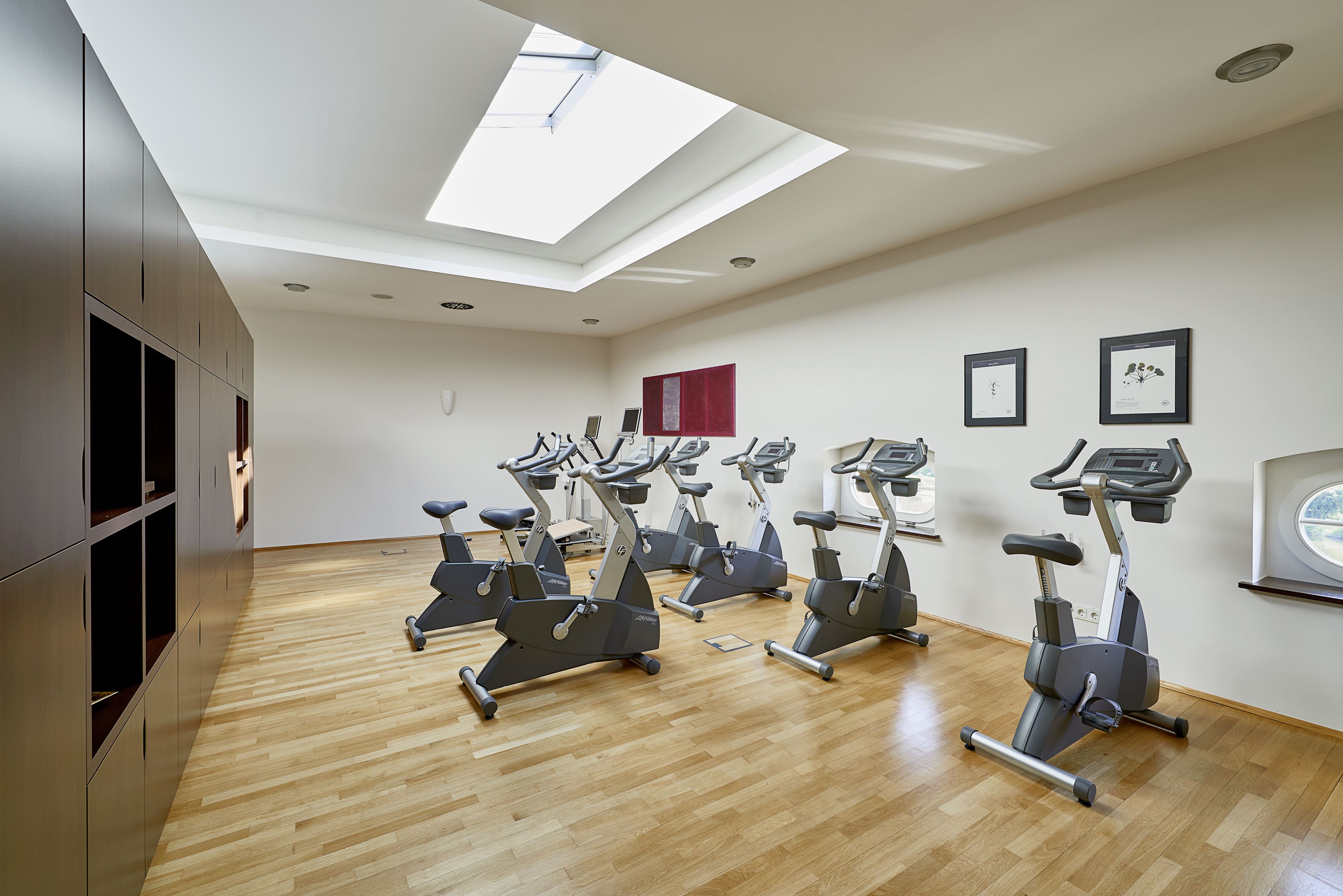 A gym with multiple exercise bikes arranged in rows, a skylight, and framed certificates on the wall.