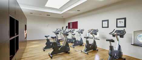 A gym with multiple exercise bikes arranged in rows, a skylight, and framed certificates on the wall.