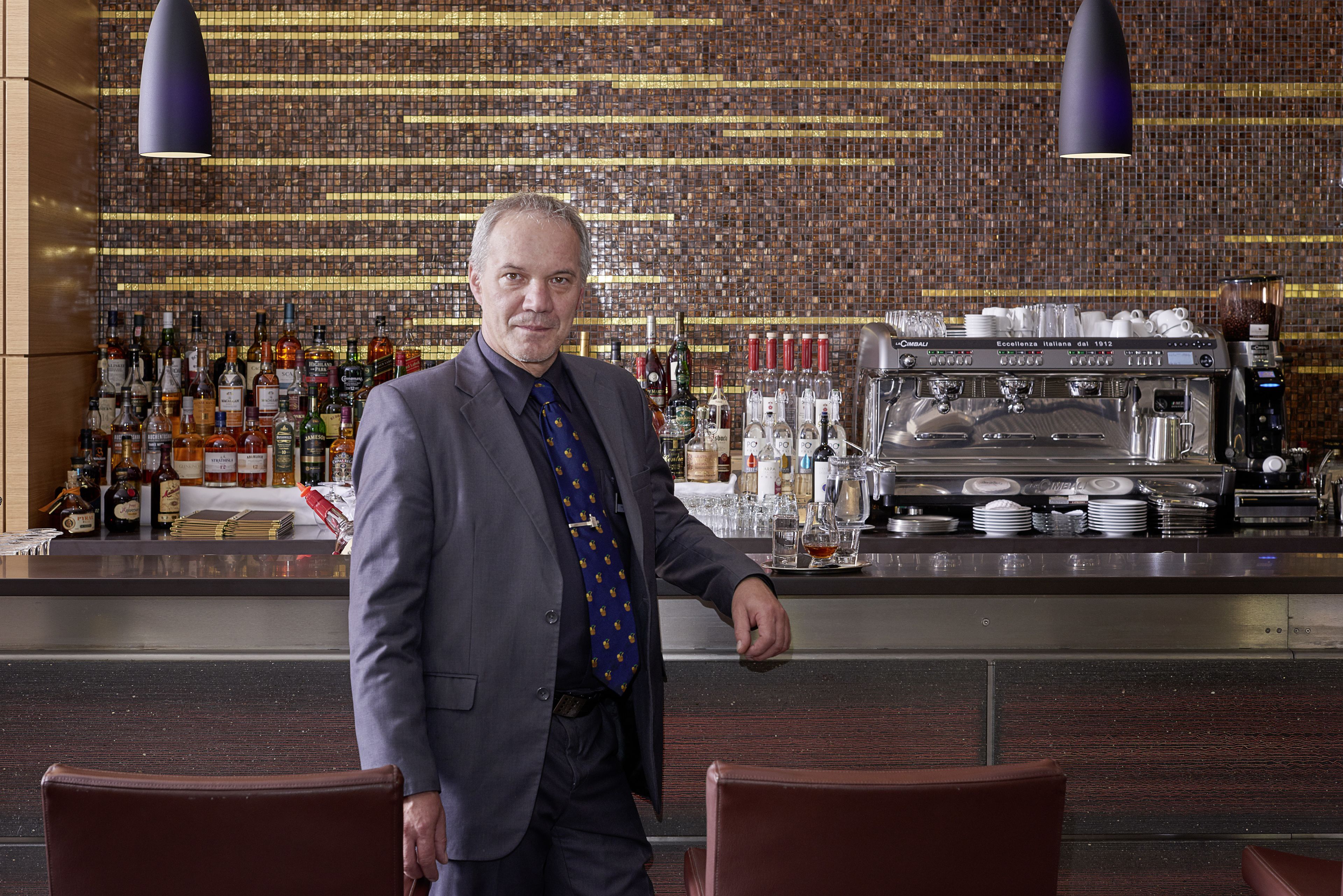 A bar area with a bartender, shelves of liquor bottles, and a coffee machine.