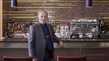 Zona de bar con un cantinero, estantes llenos de botellas de licores y una máquina de café.