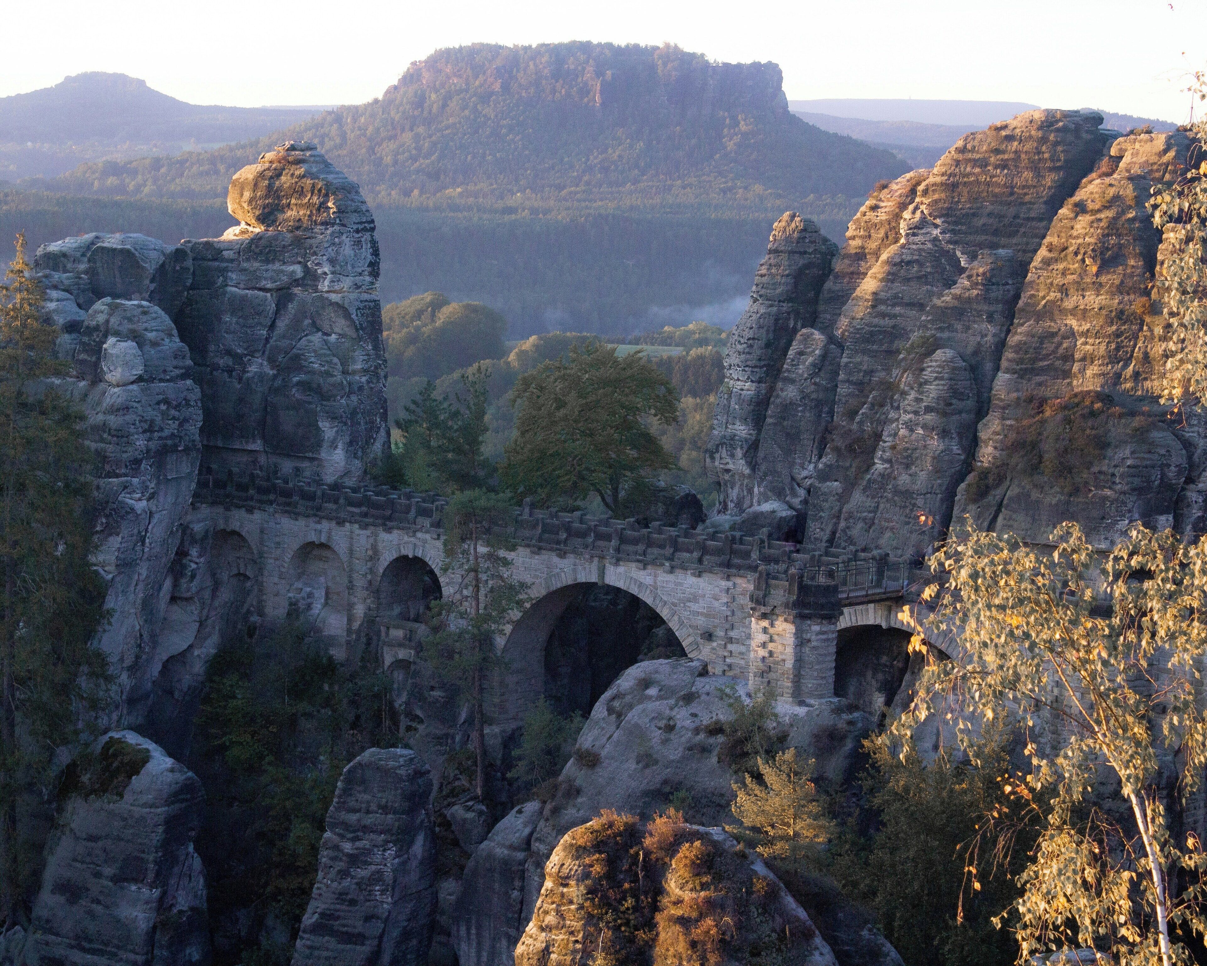 Un puente de piedra con arcos sobre un desfiladero rocoso, rodeado de colinas boscosas.