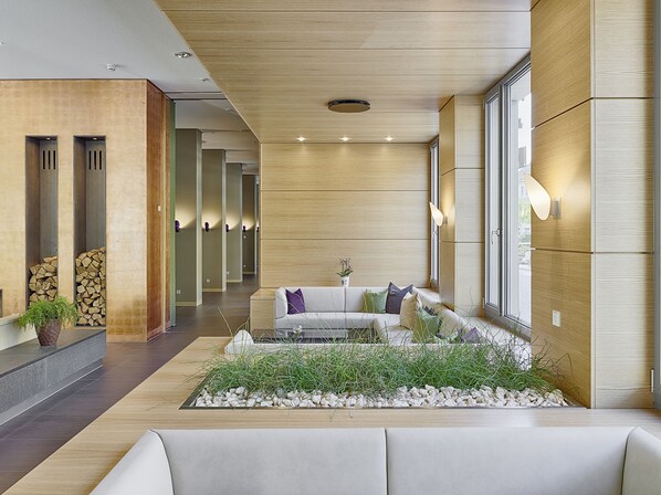 A modern lobby with a reception desk, a seating area with a sofa and cushions, a decorative plant, and a wall-mounted light fixture.