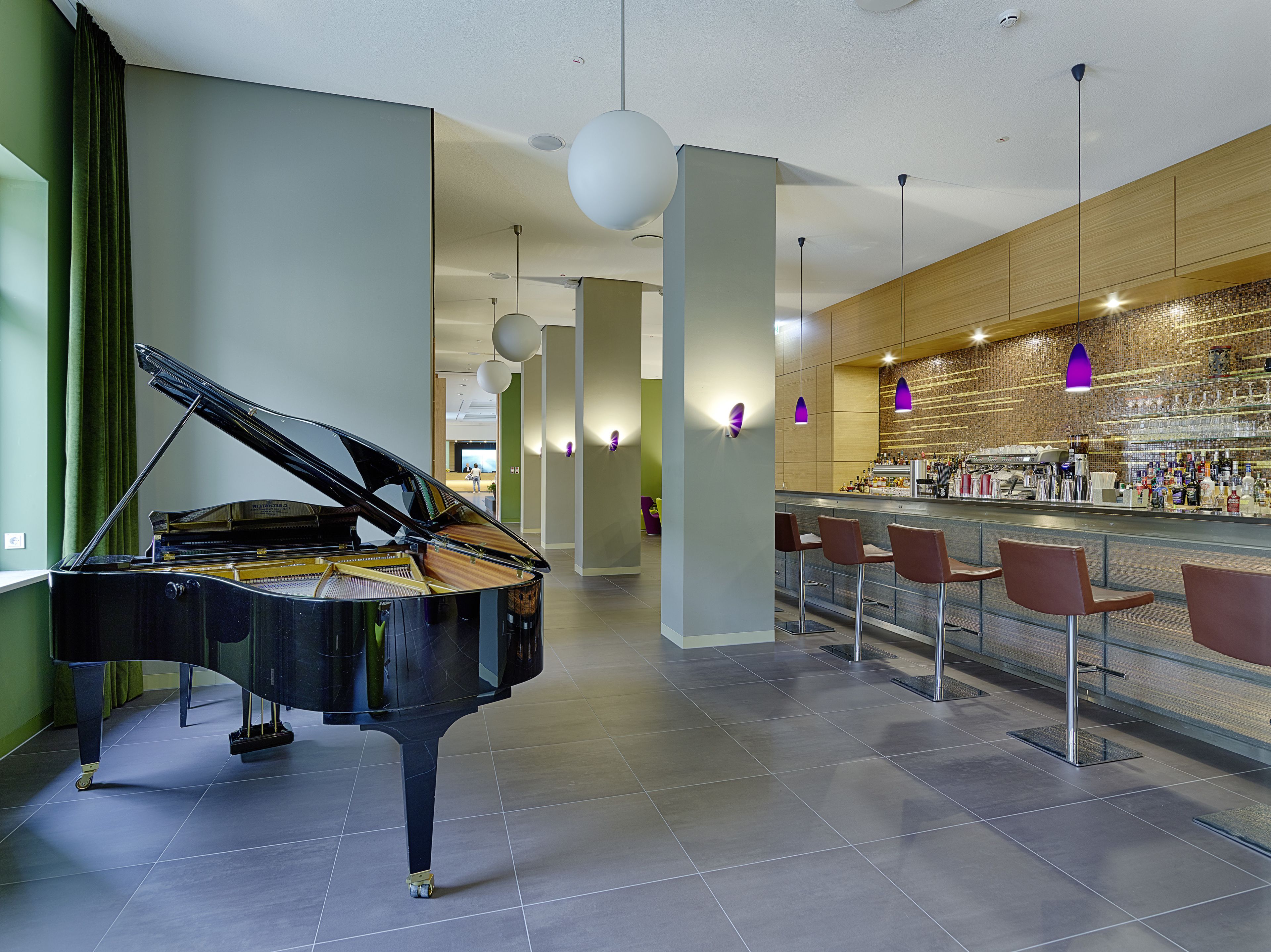 A grand piano in a spacious lobby with a bar area and modern lighting.