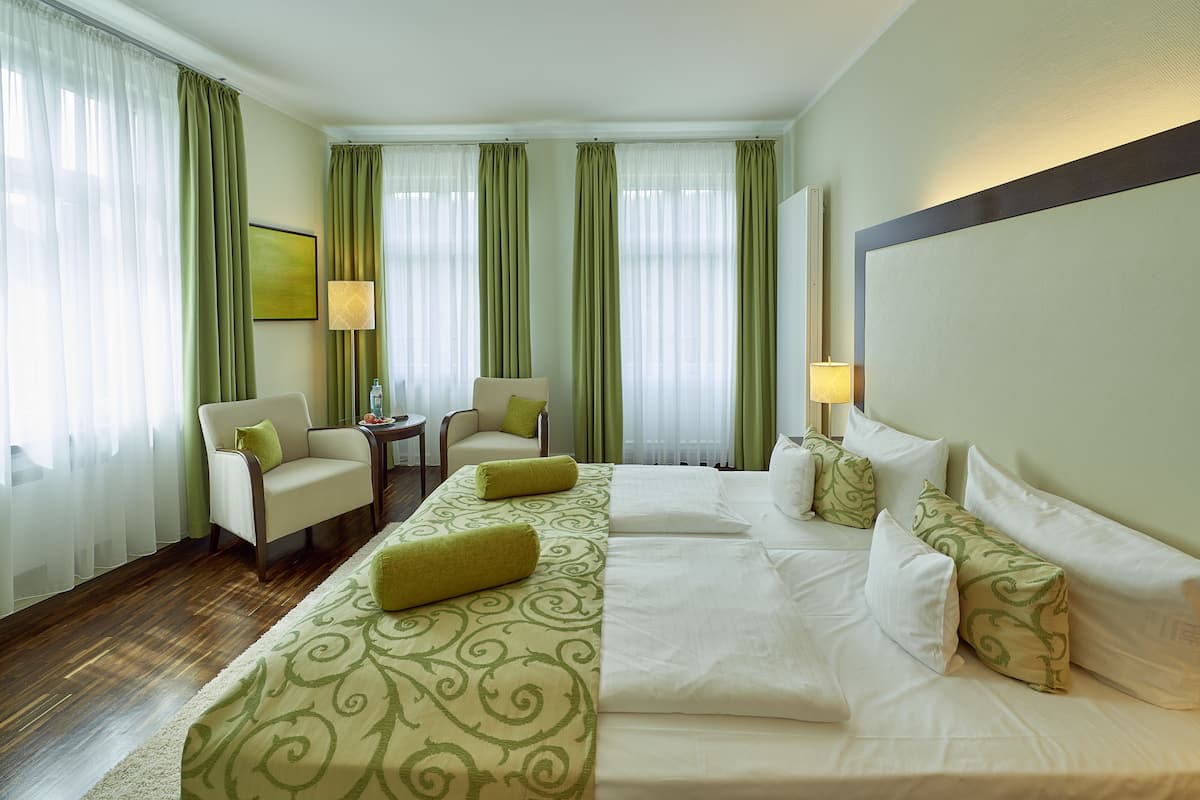 A hotel room with a large bed, two chairs, a small table, and a lamp.
