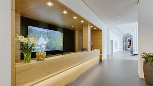 A modern reception desk with a wooden finish, a large flat-screen TV, and a vase with flowers. - Hotel Elbresidenz an der Therme Bad Schandau (Bad Schandau)