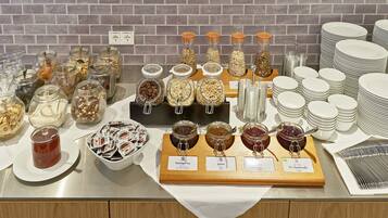 A buffet table with various food items and condiments, including jars of nuts and spreads, neatly arranged on a wooden board.
