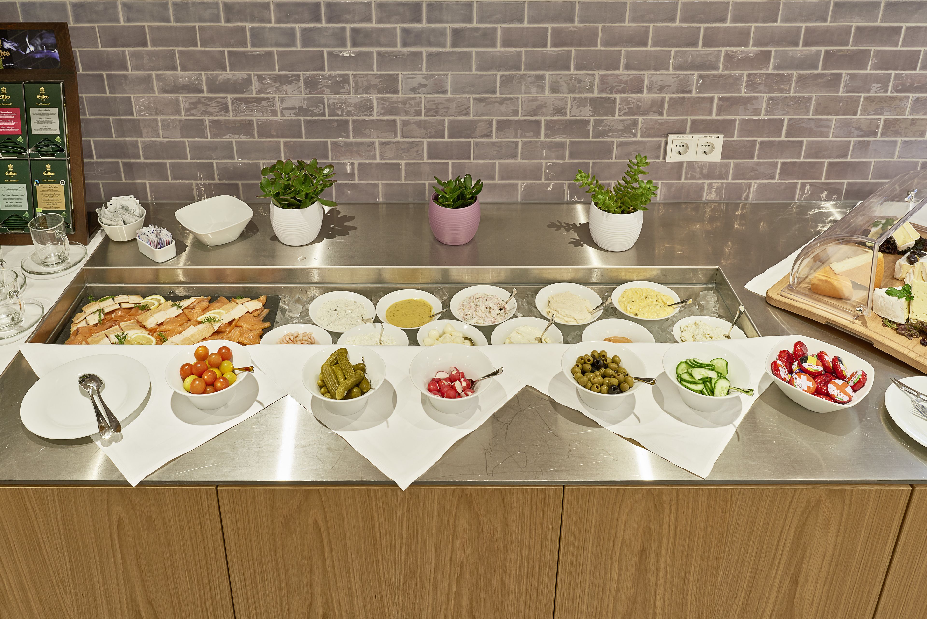 A buffet setup with various food items and small potted plants on a stainless steel counter.