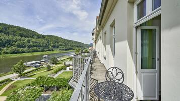 Ein Balkon mit Blick auf einen Fluss und Hügel, ein Tisch und eine Tür.