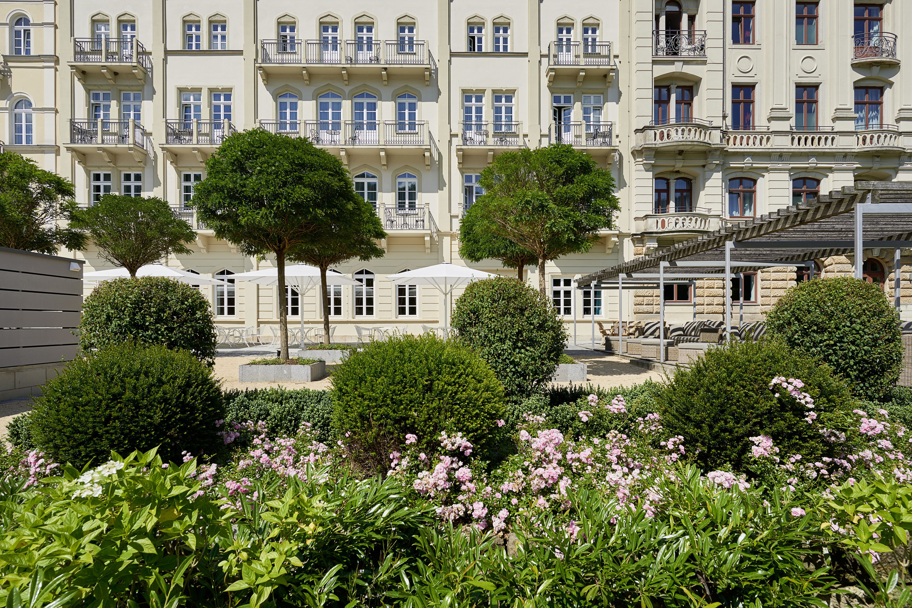 Un edificio de varios pisos con balcones y un patio con árboles y flores.