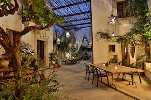 Een terras buiten met een houten tafel en stoelen, omringd door plantenbakken en lantaarns.