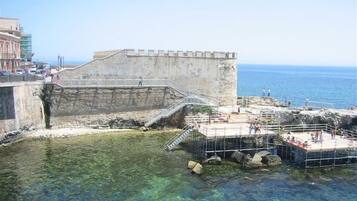 A coastal fortification with clear water in front, a staircase leading up to the fort, and a view of the sea.