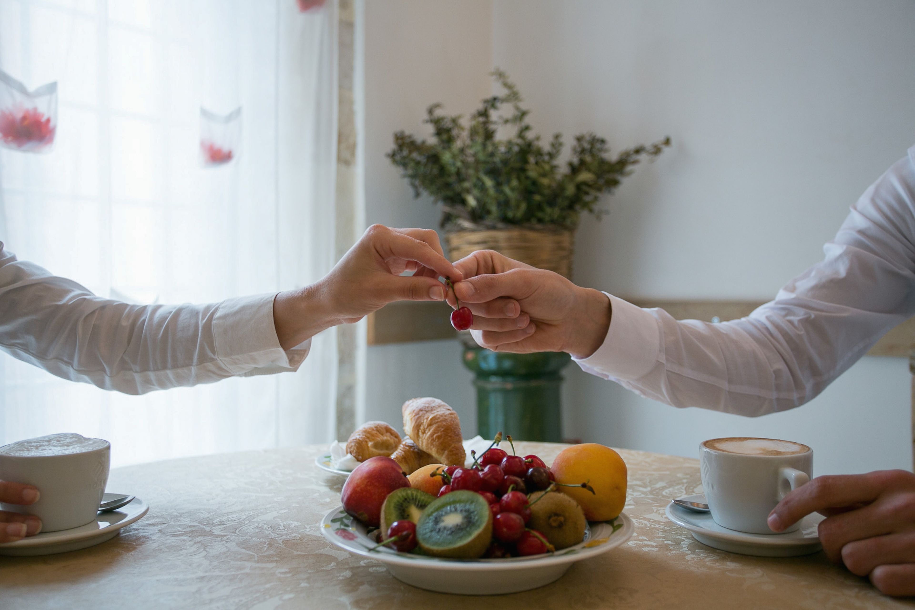 Een ontbijtsetting met een bord fruit en gebak, een kop koffie, en een decoratieve plant op de achtergrond.