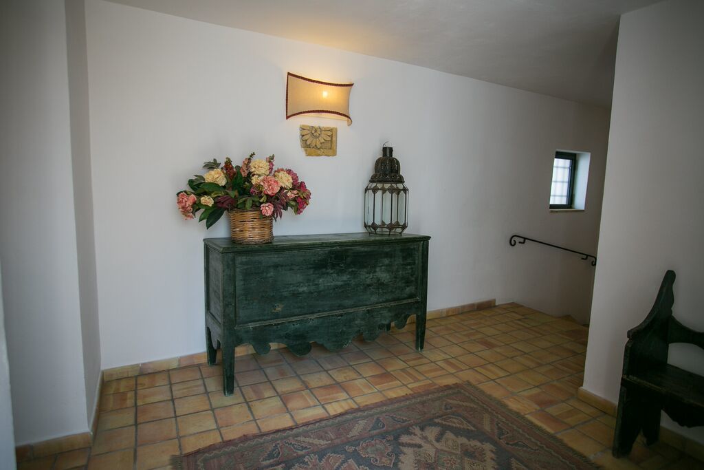 A hallway with a green console table, a wicker basket with flowers, a lantern, and a small window.