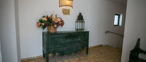 A hallway with a green console table, a wicker basket with flowers, a lantern, and a small window.