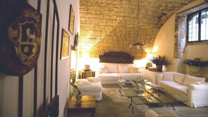 A cozy living room with a stone ceiling, white sofas, a glass coffee table, and decorative items. - Alla Giudecca (Syracuse)