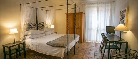 A four-poster bed with a wooden headboard, a desk with a chair, and a small table with a lamp.