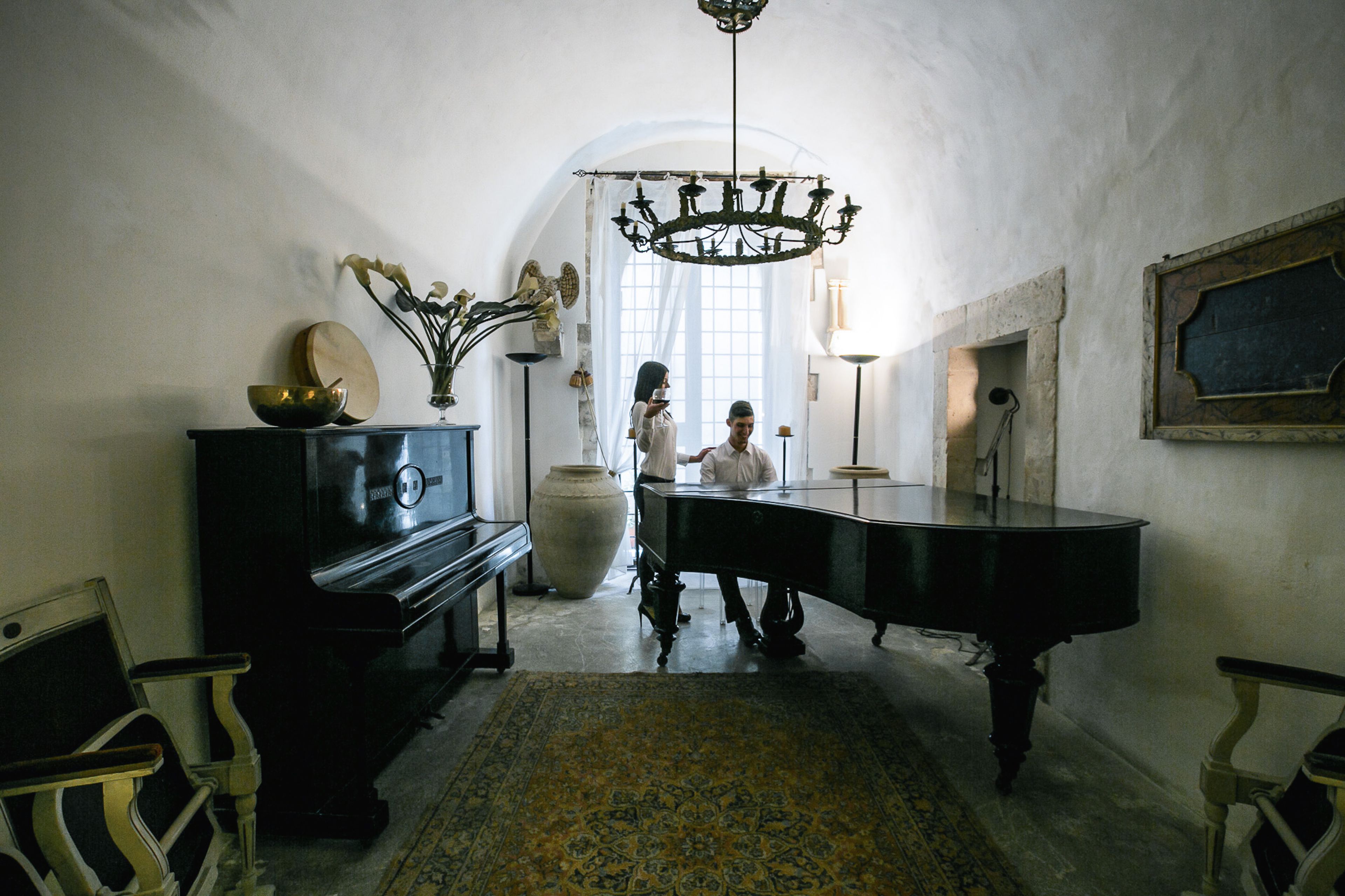 Une pièce avec un grand piano, un grand vase rempli de fleurs et un lustre.