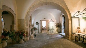 An interior with arched stone ceilings, a central doorway, and a display case with items. - Alla Giudecca (Syracuse)