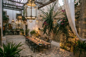 An outdoor dining area with a wooden table, chairs, hanging lanterns, and potted plants. - Alla Giudecca (Syracuse)