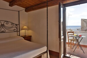Un dormitorio con una cama, una mesita de noche con lámpara y un balcón con mesa y sillas.