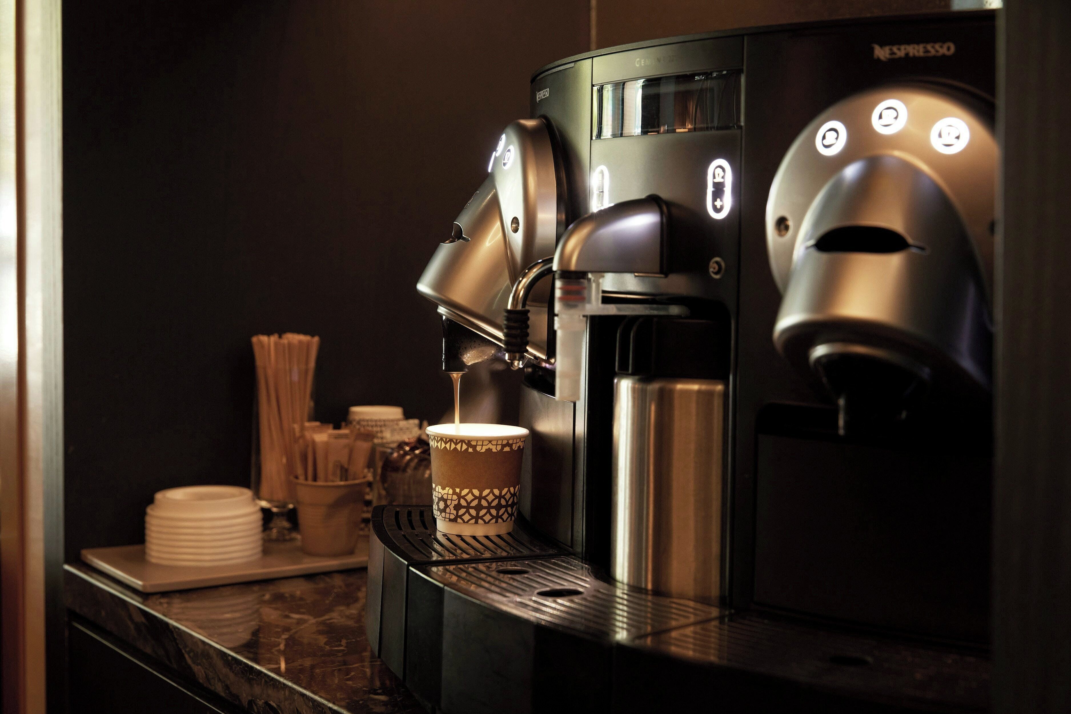 Una cafetera con una taza debajo, una pila de platos y un recipiente con utensilios sobre una encimera.