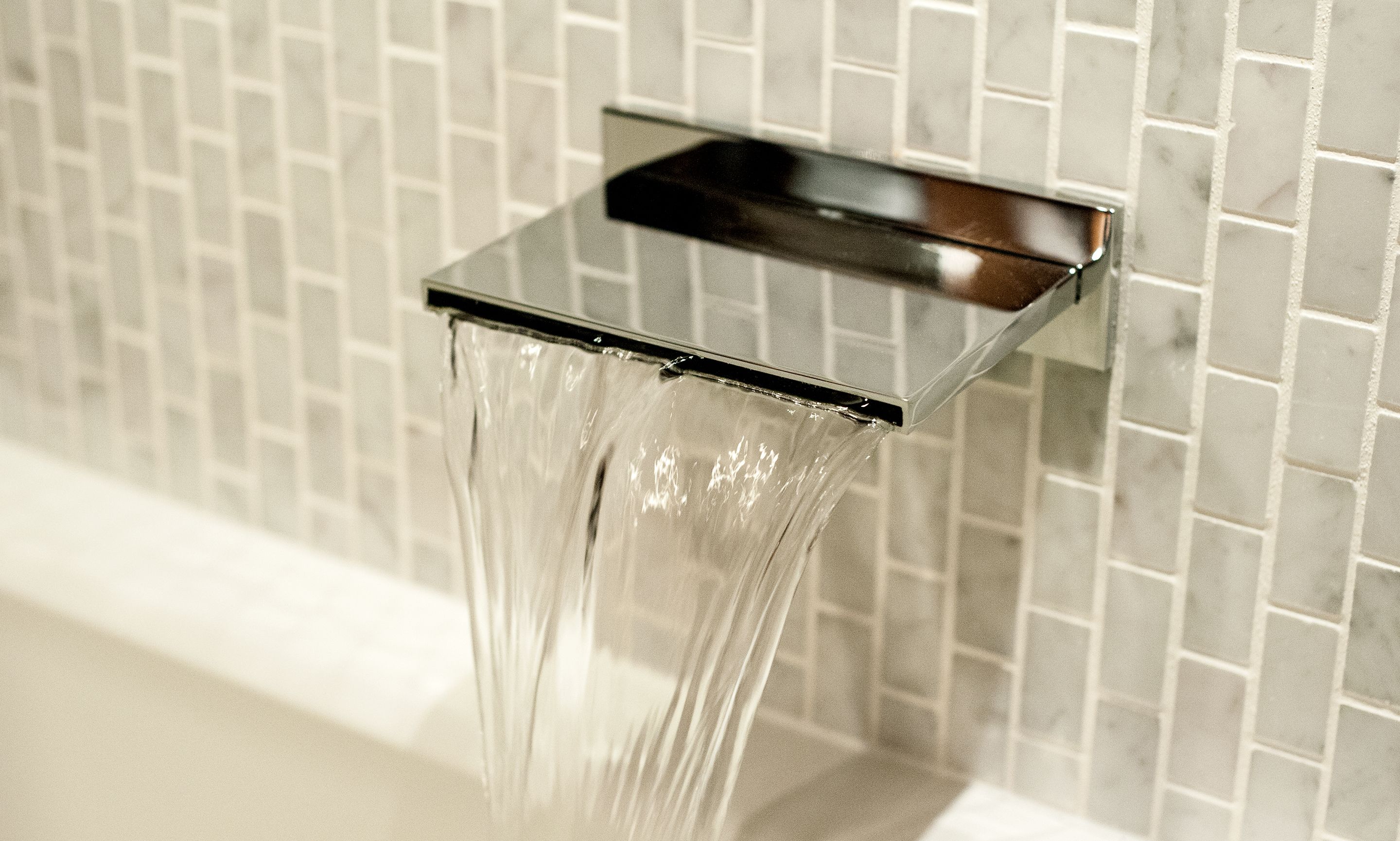 Un baño moderno con un grifo metálico cuadrado y agua cristalina corriendo.