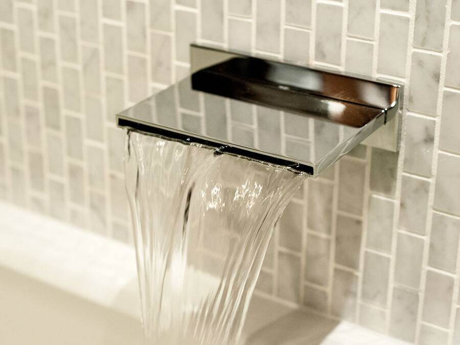Un baño moderno con un grifo metálico cuadrado y agua cristalina corriendo.