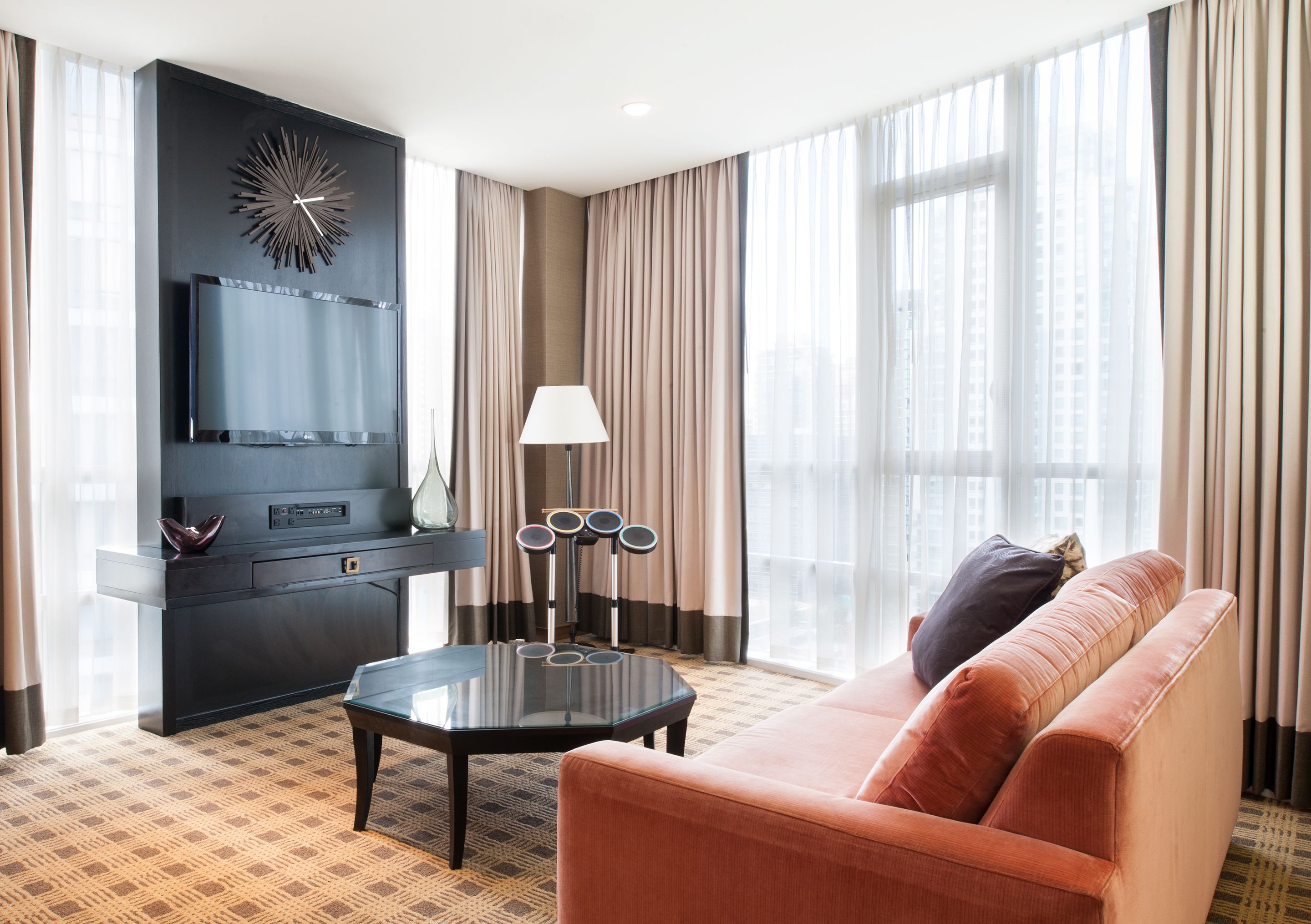 A modern hotel room with a large window, a sofa, a coffee table, a TV, and a decorative wall piece.